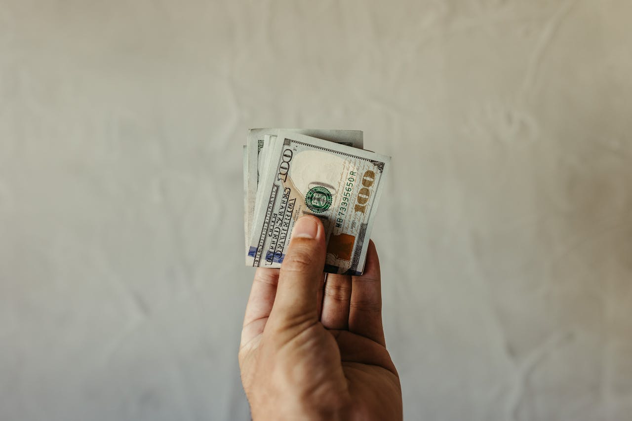 A clear view of a human hand holding a stack of US dollar bills, symbolizing finances.